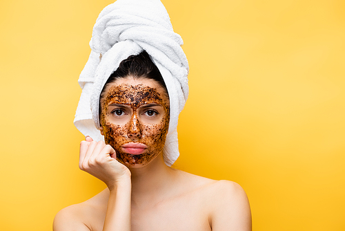 sad beautiful woman with towel on head and coffee mask on face isolated on yellow