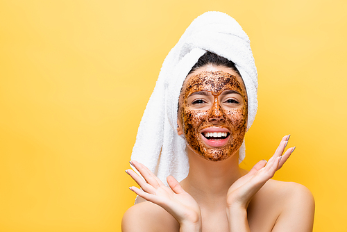happy beautiful woman with towel on head and coffee mask on face isolated on yellow