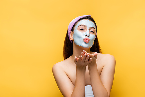 beautiful woman with clay mask on face blowing kiss isolated on yellow