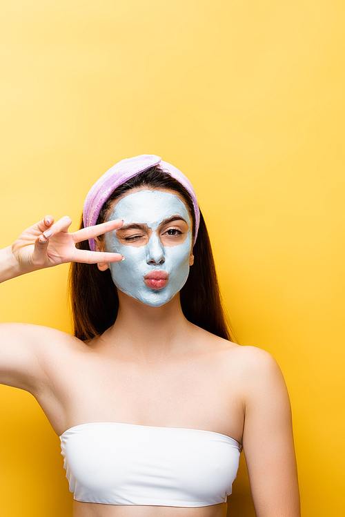 beautiful woman with clay mask on face grimacing isolated on yellow