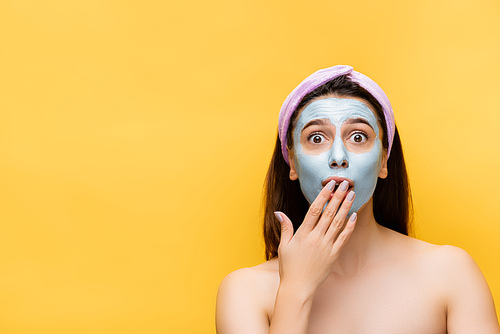 shocked beautiful woman with clay mask on face isolated on yellow