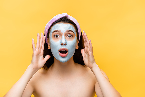 shocked beautiful woman with clay mask on face isolated on yellow