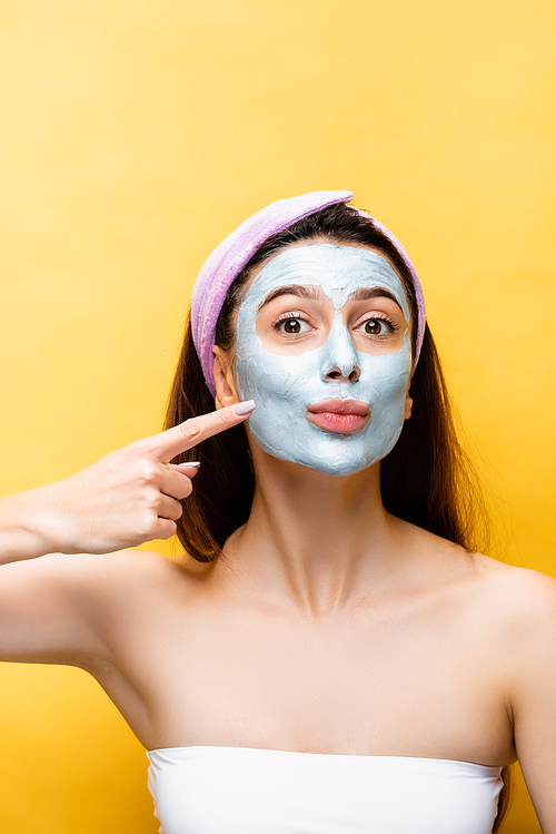 beautiful woman pointing at clay mask on face isolated on yellow