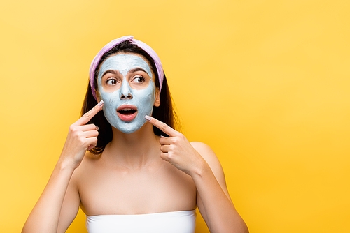 shocked beautiful woman pointing at clay mask on face isolated on yellow