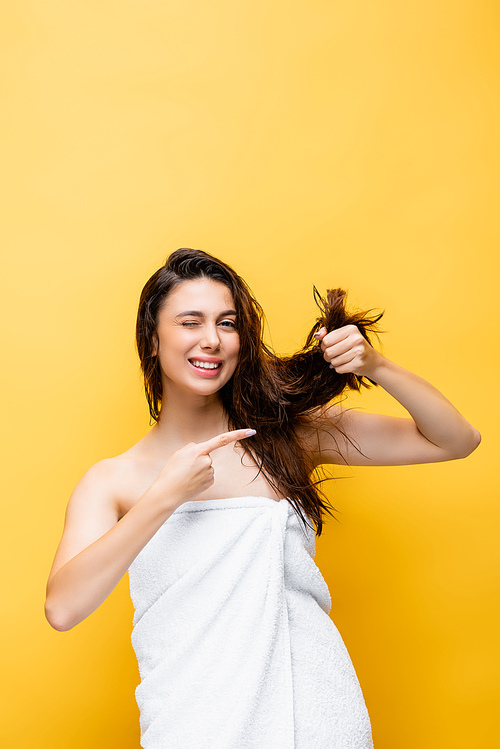 smiling beautiful woman pointing at hair isolated on yellow