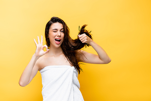beautiful woman holding hair and showing ok isolated on yellow