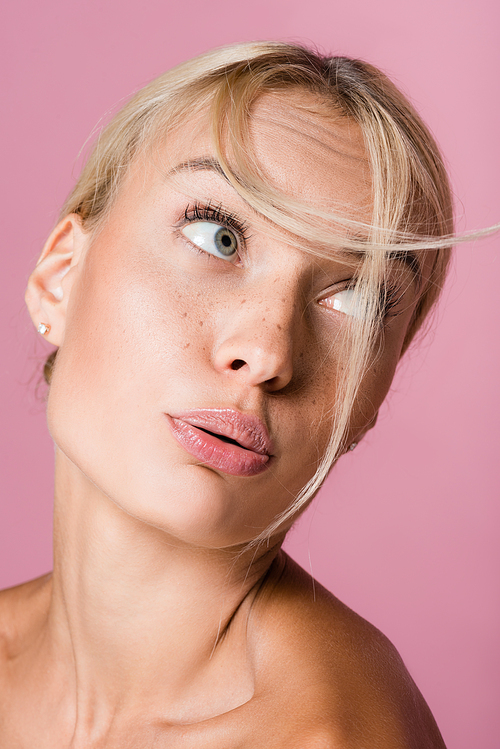 beautiful blonde woman with freckles blowing on hair isolated on pink