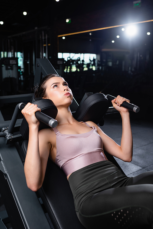 young, sportive woman training on arms extension machine in gym