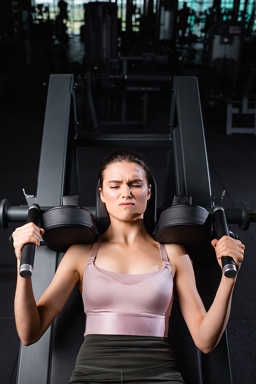 top view of sportswoman with closed eyes training on arms extension machine in gym