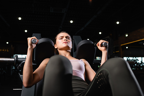 young sportswoman exercising on arm extension machine in sports center on blurred foreground