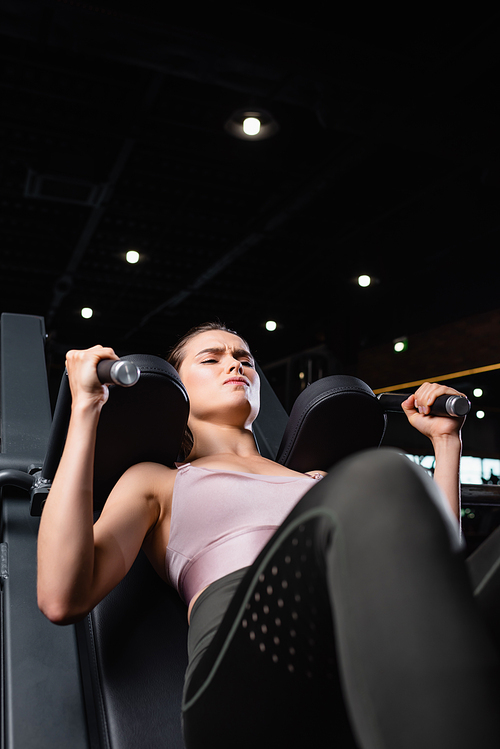 athletic sportswoman doing arms extension exercise on training machine on blurred foreground