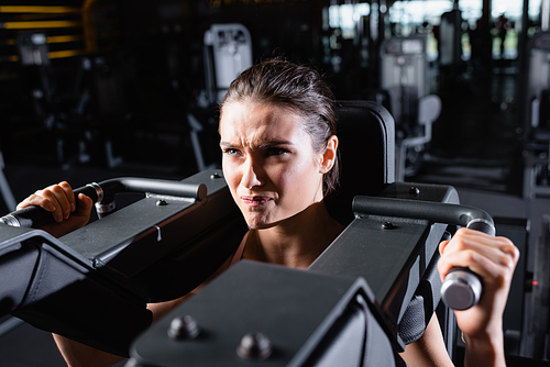 tense sportswoman working out on arms extension machine in gym