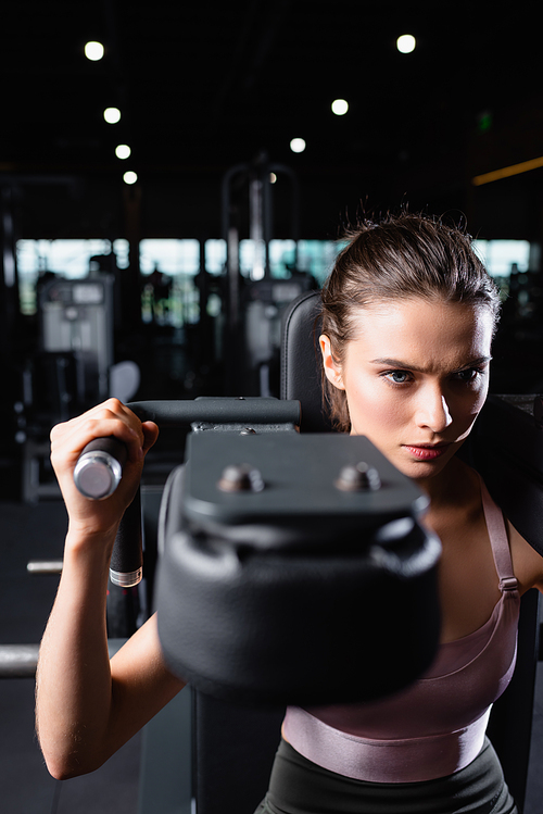 sportive woman doing arms extension exercise on training machine on blurred foreground