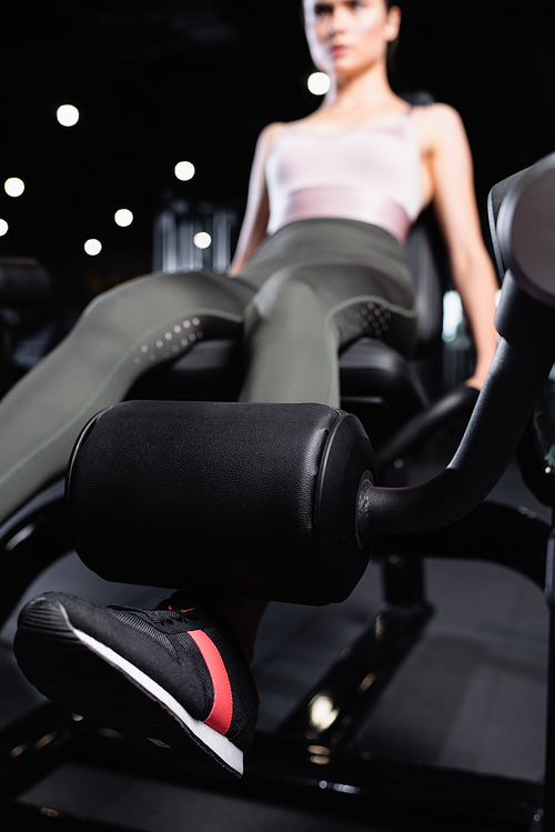 young sportswoman doing leg extension exercise on training machine on blurred background