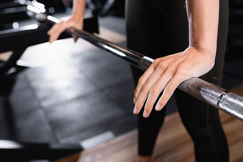 cropped view of sportswoman touching power rack on blurred background