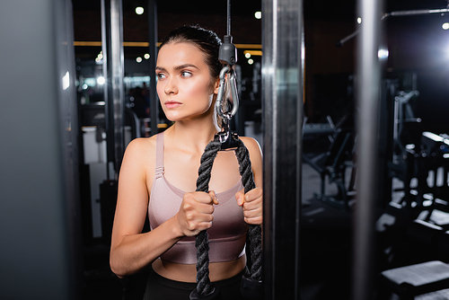 athletic sportswoman looking away while exercising on cable pushdown machine on blurred foreground