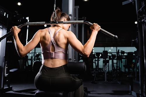 back view of athletic sportswoman doing back and arms extension exercise on lat machine