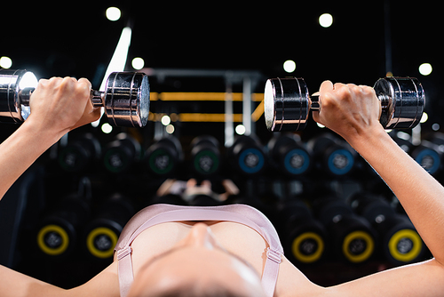 sportswoman exercising with dumbbells in lying position on blurred foreground