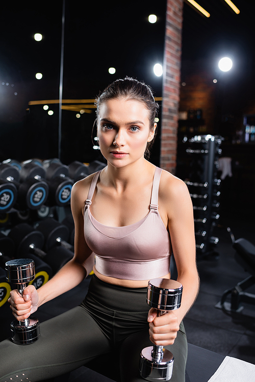 athletic sportswoman holding dumbbells and  while sitting in gym