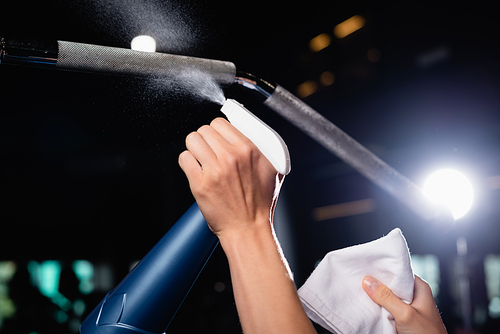 partial view of charwoman spraying detergent on sports equipment in gym