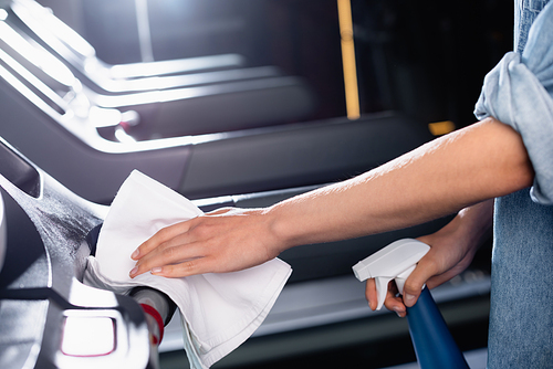 cropped view of charwoman holding spray bottle while wiping treadmill in sports center on blurred background