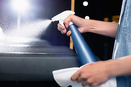 partial view of charwoman spraying detergent on treadmill in sports center