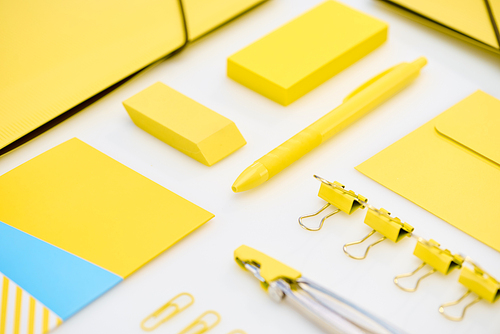 flat lay of yellow paper clips, compasses, envelope, pen, yellow and blue stickers, folders and eraser