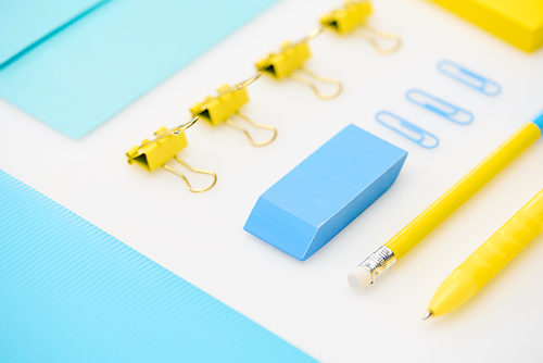 flat lay of blue eraser, paper clips, folder, envelope, yellow pen, pencil, stickers in white background
