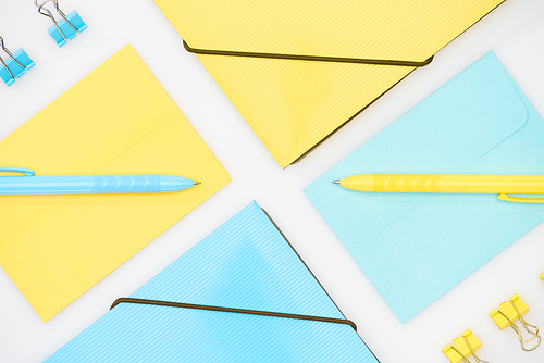 flat lay of blue and yellow folders, envelopes, paper clips and pens isolated on white