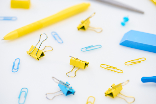 selective focus of yellow and blue paper clips with pen, eraser, scissors and pencil sharpener on white background