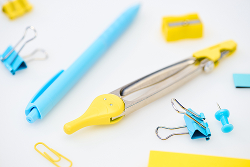 selective focus of yellow and blue stationery with paper clips, compasses, pencil sharpener and pen on white background
