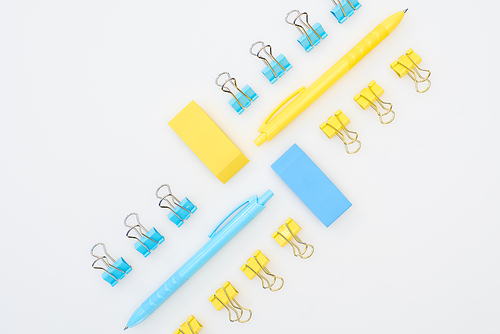 flat lay of yellow and blue erasers, pens and paper clips isolated on white