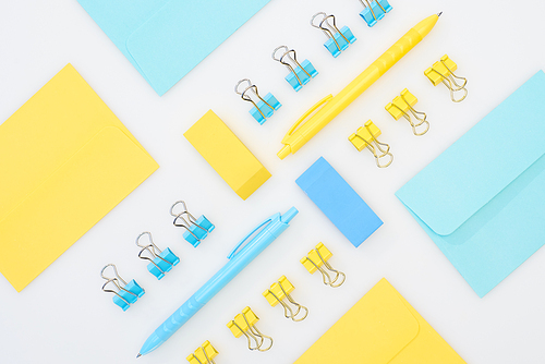 flat lay of yellow and blue erasers, pens, envelopes and paper clips isolated on white