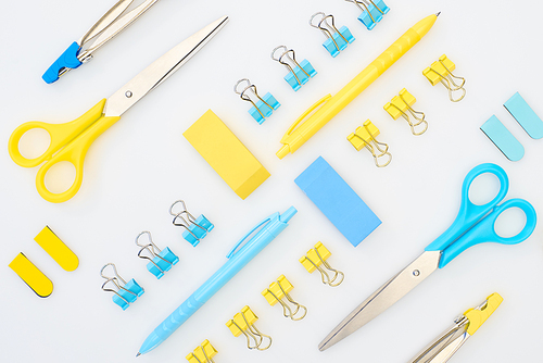 flat lay of yellow and blue erasers, pens, scissors, compasses and paper clips isolated on white