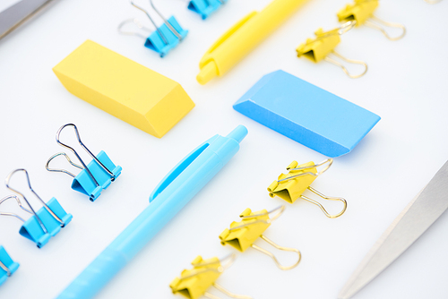 selective focus of yellow and blue erasers, pens, paper clips and scissors isolated on white