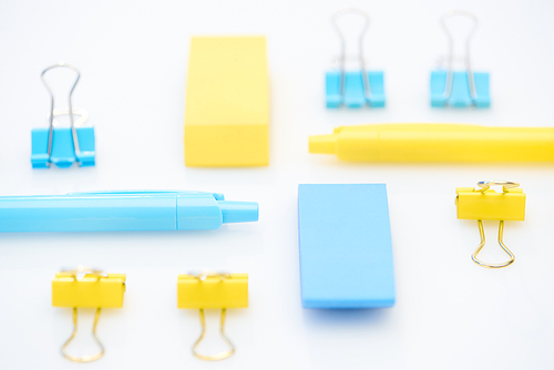 selective focus of yellow and blue pencils, erasers and paper clips on white background