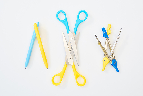 top view of yellow and blue scissors, pens and compasses on white background