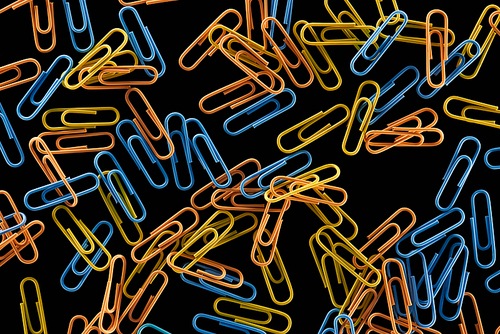 top view of small yellow, orange and blue paper clips isolated on black