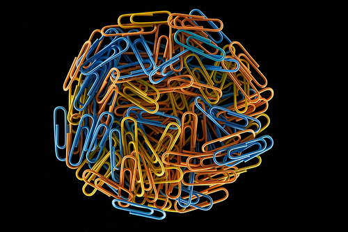 top view of yellow, blue and orange paper clips in circle isolated on black
