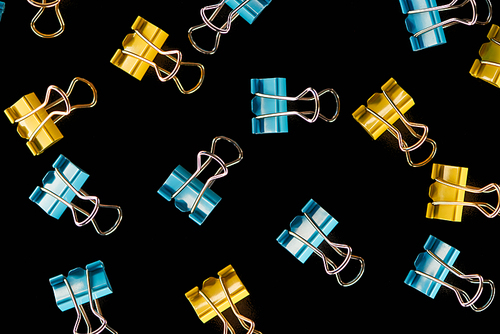 top view of colorful scattered yellow, orange and blue paper clips isolated on black