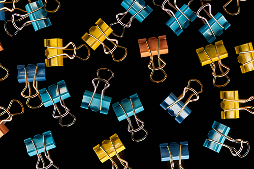 top view of colorful, small, scattered yellow, orange and blue paper clips isolated on black