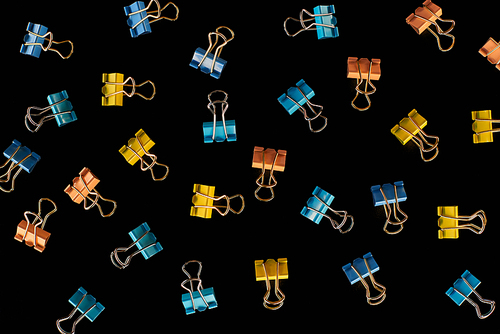 top view of scattered yellow, orange and blue paper clips isolated on black