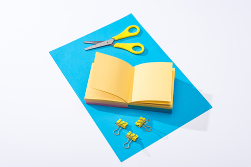 high angle view of notebook, scissors, binder clips and paper on white background