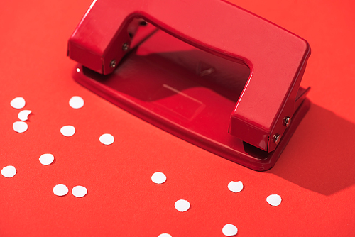 high angle view of holepunch with paper circles on red background