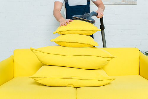 cropped view of cleaner removing dust on stacked pillows with vacuum cleaner