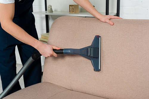 cropped view of cleaner in uniform dry cleaning modern sofa with vacuum cleaner