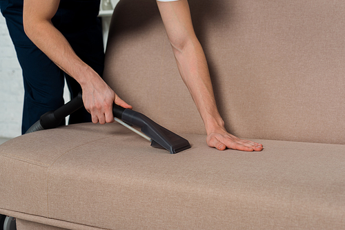 cropped view of man cleaning modern sofa with vacuum cleaner