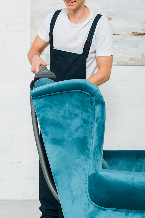 cropped view of happy cleaner washing modern armchair with vacuum cleaner