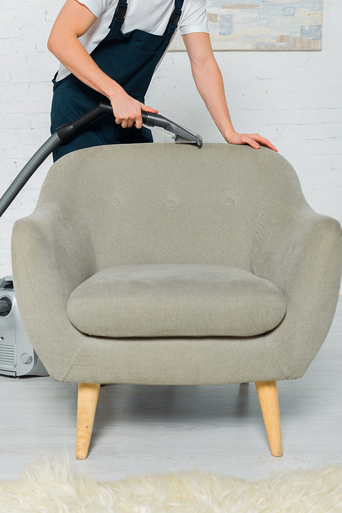 cropped view of cleaner in uniform dry cleaning armchair with vacuum cleaner