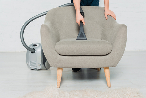 cropped view of young man dry cleaning armchair with modern vacuum cleaner
